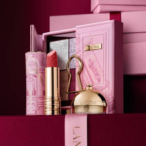 A curated Lancome holiday gift set featuring a lipstick, eyeshadow palette, and gold beauty products displayed against a decorative pink case.